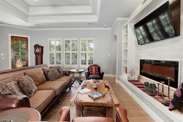 living room featuring built in shelves, a tray ceiling, hardwood / wood-style flooring, and ornamental molding