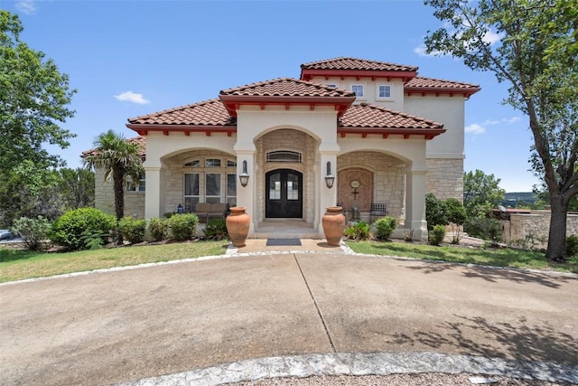 mediterranean / spanish house featuring a tile roof, french doors, stone siding, and stucco siding