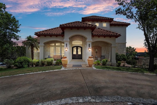 mediterranean / spanish-style home featuring french doors, stone siding, a tile roof, and stucco siding