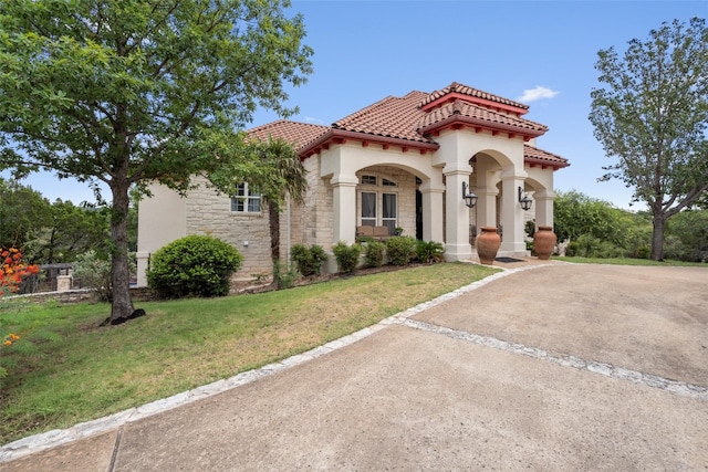 mediterranean / spanish-style house with a front yard, a tiled roof, stone siding, and stucco siding