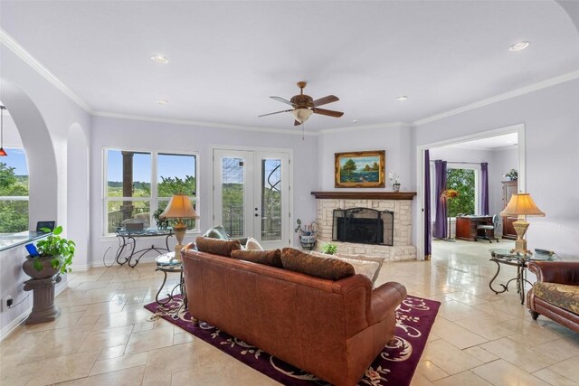 tiled living room with a stone fireplace, french doors, crown molding, and ceiling fan