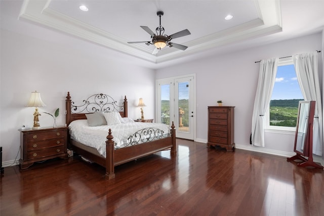 bedroom with ceiling fan, a tray ceiling, hardwood / wood-style flooring, and multiple windows