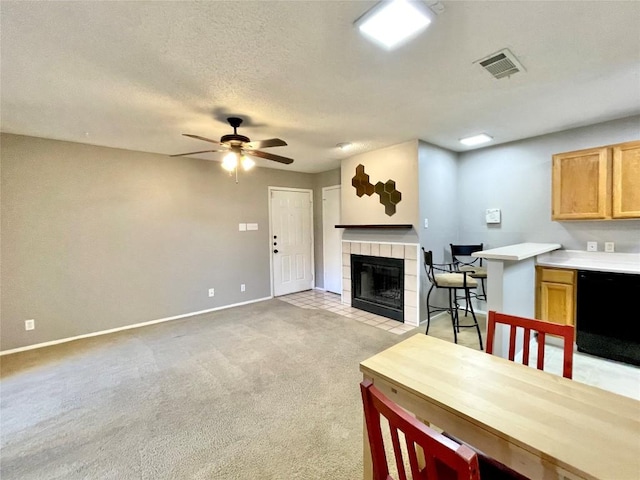 living room featuring ceiling fan, a tiled fireplace, light carpet, and a textured ceiling