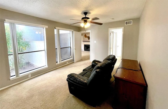 carpeted living room featuring ceiling fan, plenty of natural light, a tiled fireplace, and a textured ceiling