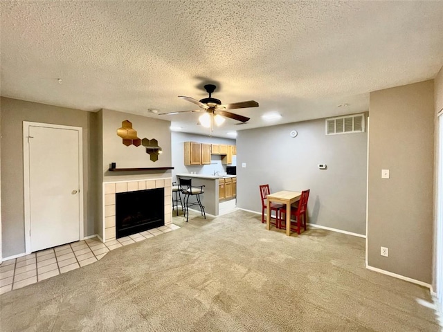 living room with a textured ceiling, a fireplace, light colored carpet, and ceiling fan