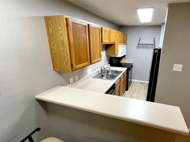 kitchen featuring kitchen peninsula, sink, light hardwood / wood-style flooring, and black appliances