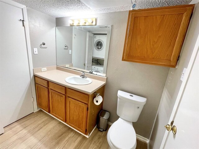 bathroom with wood-type flooring, stacked washer and dryer, vanity, toilet, and a textured ceiling