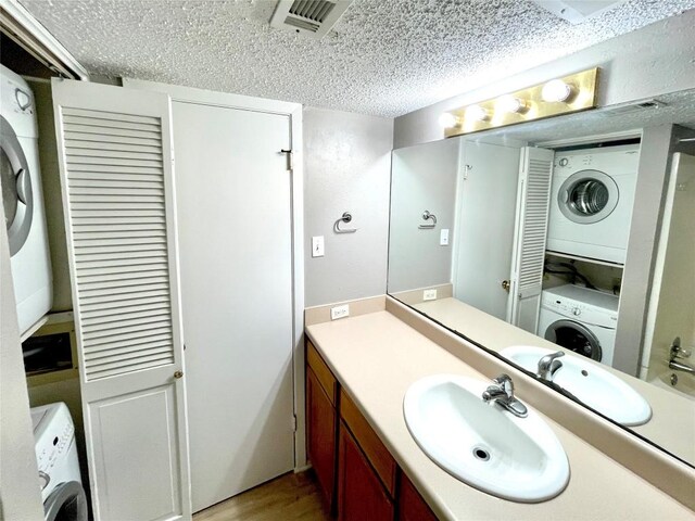 bathroom featuring vanity, stacked washer / drying machine, wood-type flooring, and a textured ceiling