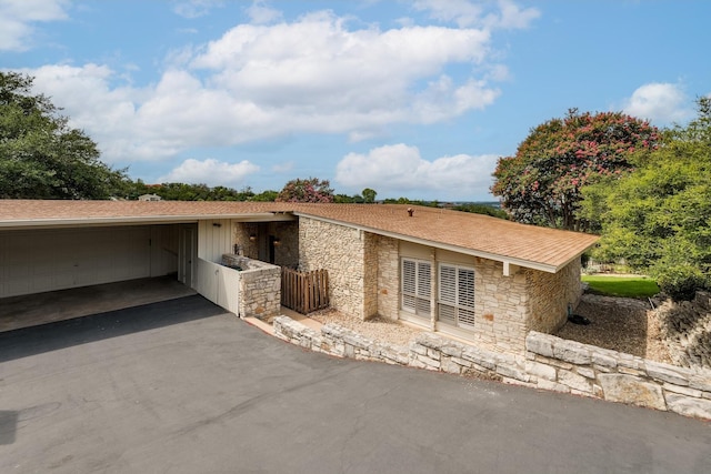 view of side of home featuring driveway, stone siding, and a shingled roof