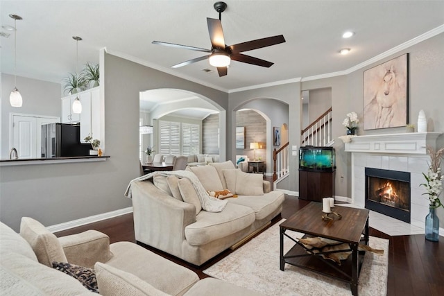 living room featuring dark hardwood / wood-style floors, ceiling fan, crown molding, and a tiled fireplace