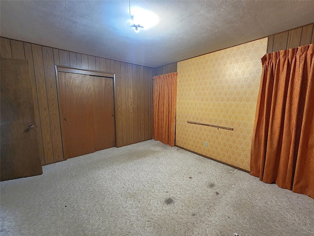 spare room featuring a textured ceiling, light carpet, and wood walls