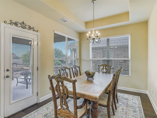 dining space with a notable chandelier, a tray ceiling, and dark hardwood / wood-style flooring