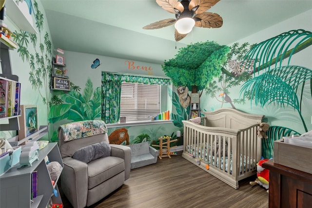 bedroom featuring dark hardwood / wood-style flooring, a crib, and ceiling fan