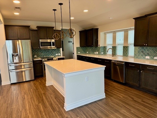 kitchen featuring tasteful backsplash, stainless steel appliances, decorative light fixtures, a kitchen island, and dark hardwood / wood-style floors