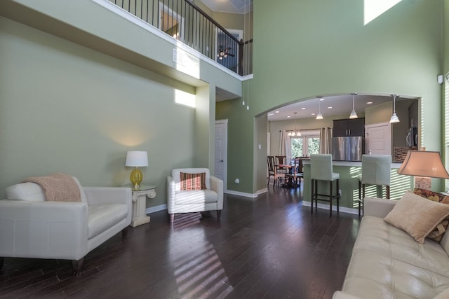 living room featuring arched walkways, a towering ceiling, baseboards, and wood finished floors