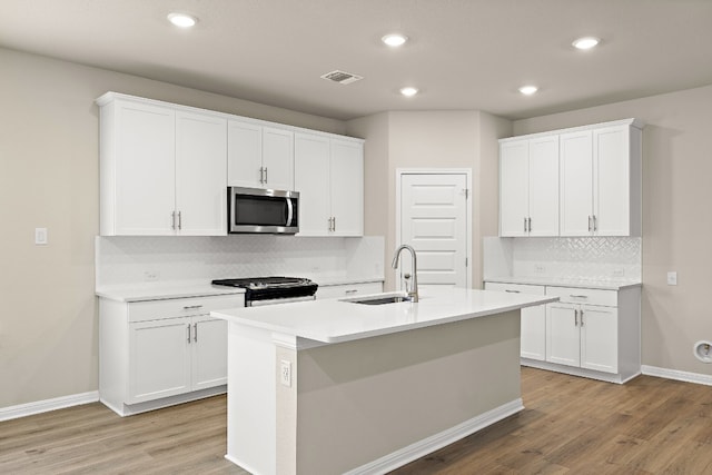 kitchen featuring gas range, tasteful backsplash, sink, a center island with sink, and light wood-type flooring