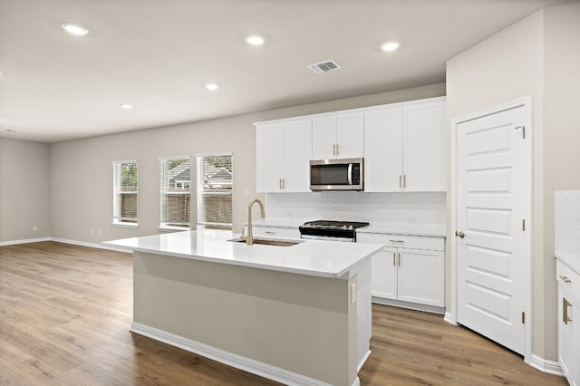 kitchen with tasteful backsplash, a kitchen island with sink, light hardwood / wood-style floors, sink, and stainless steel appliances