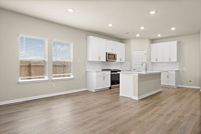 kitchen with decorative backsplash, a center island with sink, range, and light wood-type flooring