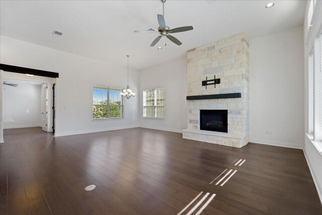 unfurnished living room featuring a stone fireplace, ceiling fan with notable chandelier, and dark hardwood / wood-style flooring