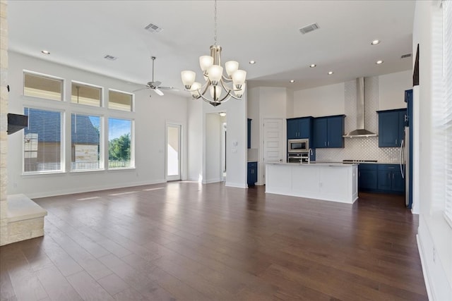 unfurnished living room with dark wood-type flooring, a towering ceiling, and ceiling fan with notable chandelier