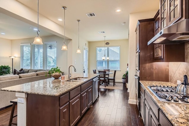 kitchen featuring dark brown cabinetry, visible vents, glass insert cabinets, under cabinet range hood, and a sink