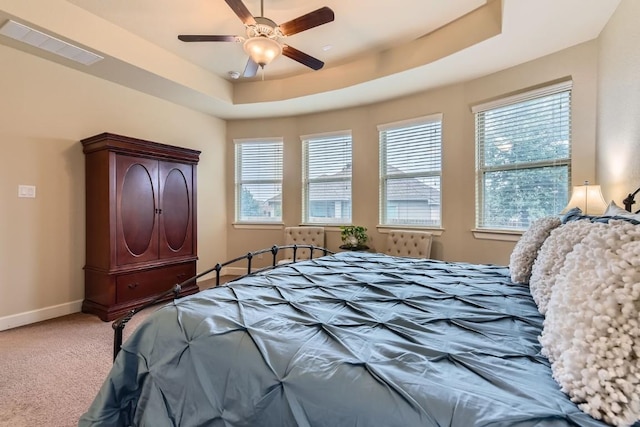 carpeted bedroom with a ceiling fan, a tray ceiling, visible vents, and baseboards