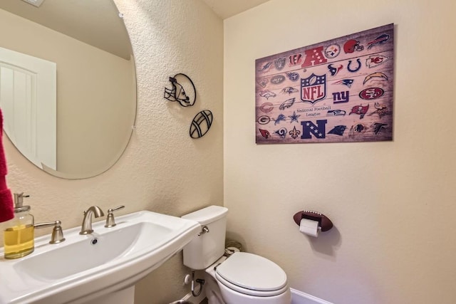 half bathroom featuring toilet, baseboards, a sink, and a textured wall