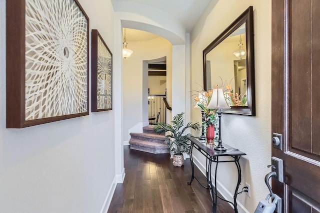 hall featuring arched walkways, dark wood-style flooring, stairs, and baseboards