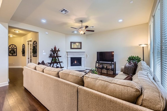 living area with a warm lit fireplace, baseboards, visible vents, dark wood finished floors, and ceiling fan