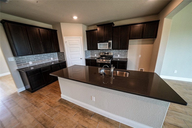 kitchen featuring decorative backsplash, appliances with stainless steel finishes, a kitchen island with sink, and sink