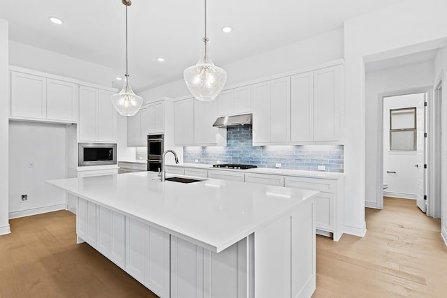 kitchen featuring appliances with stainless steel finishes, a kitchen island with sink, sink, decorative light fixtures, and white cabinets