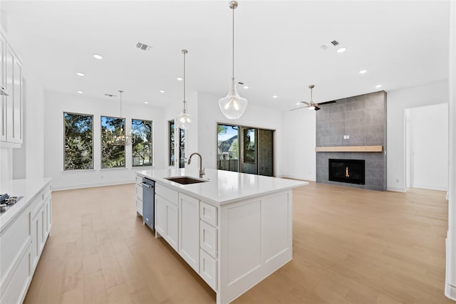 kitchen with hanging light fixtures, sink, white cabinets, a tile fireplace, and a center island with sink