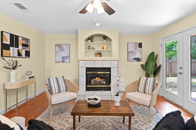 sitting room with hardwood / wood-style floors, a tile fireplace, french doors, built in shelves, and ceiling fan