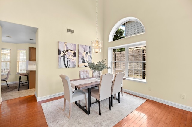 dining space featuring light wood-type flooring, a towering ceiling, and a chandelier