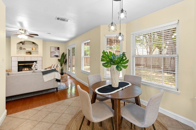 dining space with a fireplace, light tile patterned floors, built in features, and ceiling fan