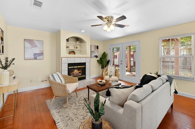 living room featuring hardwood / wood-style floors, french doors, built in shelves, ceiling fan, and a fireplace