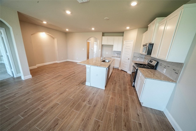 kitchen with backsplash, light stone counters, stainless steel electric stove, a center island with sink, and white cabinetry