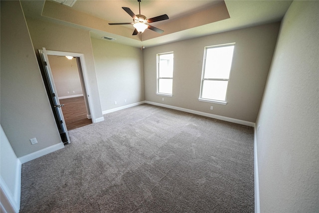 empty room featuring a raised ceiling, ceiling fan, and carpet floors