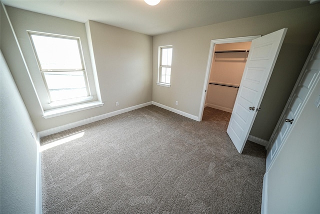 unfurnished bedroom with a spacious closet, a closet, and dark colored carpet