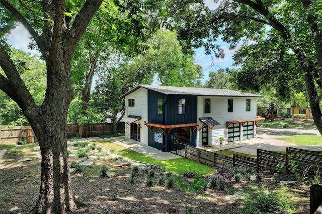 view of front of home featuring concrete driveway, board and batten siding, metal roof, a garage, and a fenced backyard