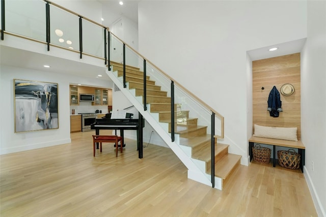 stairway featuring recessed lighting, baseboards, a high ceiling, and wood finished floors