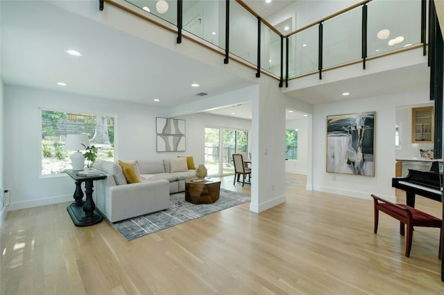 living area with recessed lighting, visible vents, light wood-style flooring, a high ceiling, and baseboards