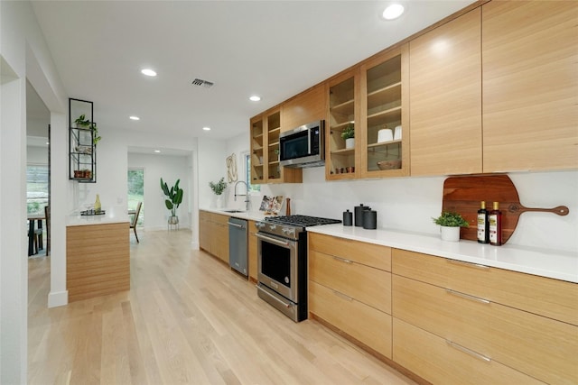 kitchen featuring stainless steel appliances, a sink, visible vents, light wood-style floors, and light countertops