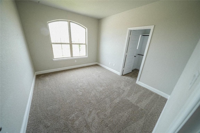 unfurnished bedroom with carpet floors, a spacious closet, baseboards, and lofted ceiling