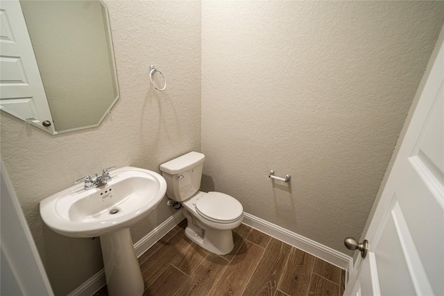 bathroom with a textured wall, toilet, wood finish floors, a sink, and baseboards