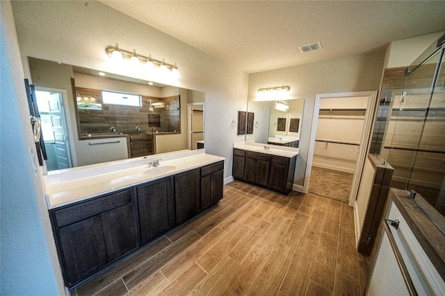 bathroom featuring a stall shower, visible vents, a sink, wood tiled floor, and two vanities