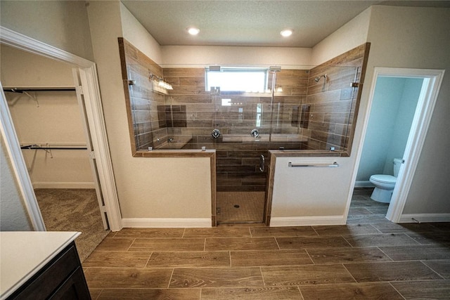 full bathroom featuring toilet, baseboards, a spacious closet, wood tiled floor, and a stall shower