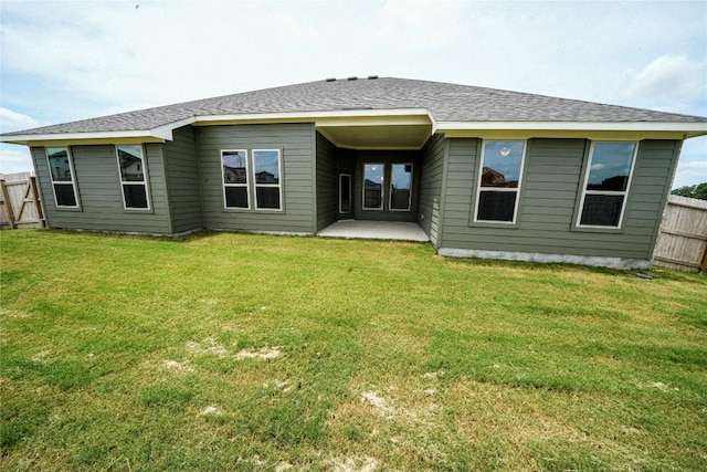 rear view of property with a shingled roof, fence, a lawn, and a patio