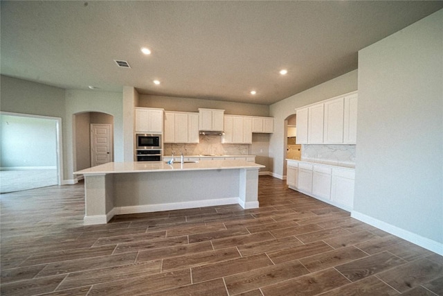 kitchen featuring arched walkways, wood finish floors, visible vents, built in microwave, and a large island with sink