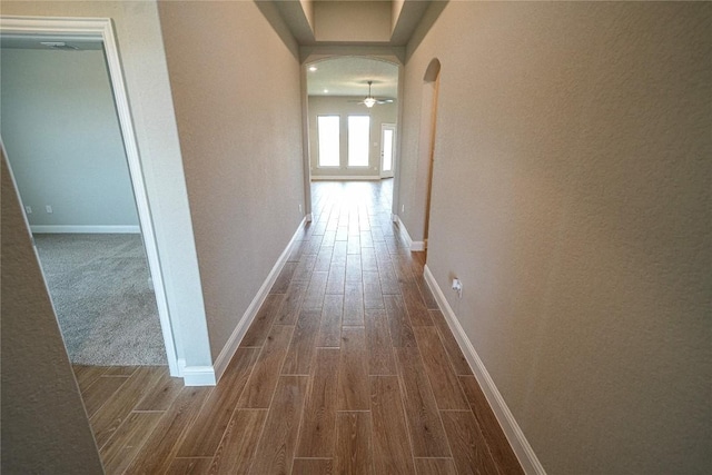 hallway featuring arched walkways, baseboards, and wood tiled floor